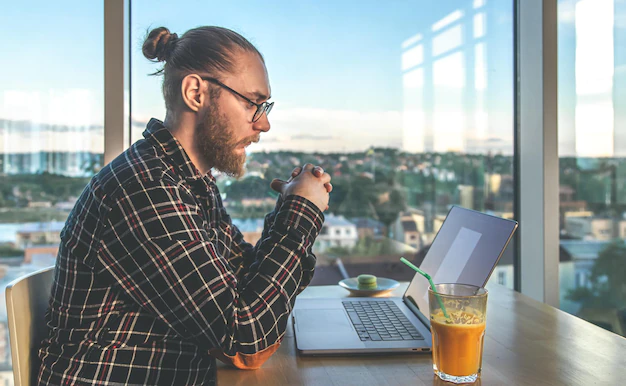 Homme barbu à lunettes et chemise à carreaux, devant son ordinanteur